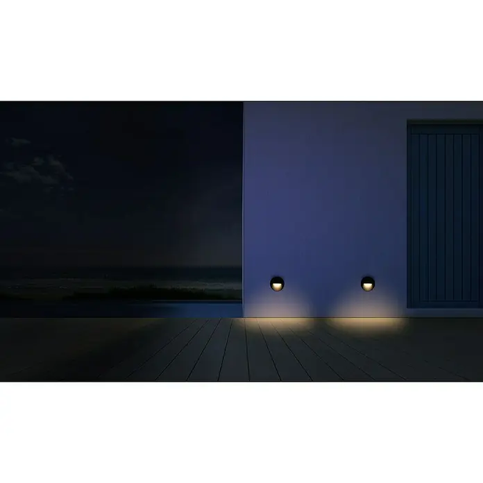 Forlight Plafón LED redondo Hide - 2,7 W, Ø x L: 14 cm x 1,5 mm, Antracita, Blanco neutro - Una escena nocturna que muestra dos luces de pared empotradas que proyectan un cálido resplandor sobre un patio de madera, mejorando la iluminación ambiental.