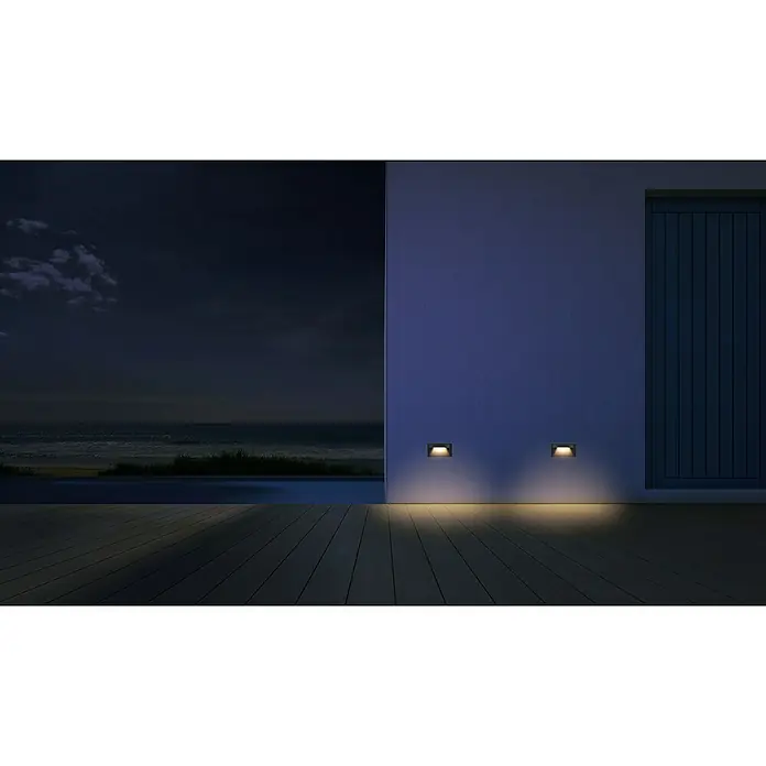 Forlight Hide Aplique exterior LED - 8 W, L x An x Al: 2,5 x 13,5 x 7,5 cm, Antracita, Blanco neutro - Escena nocturna atmosférica con luces de pared empotradas que iluminan el suelo, creando un ambiente cálido en una terraza exterior cerca del mar.