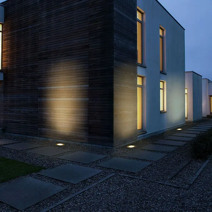 Forlight Foco empotrable Incasso - 6,2 W, Ø x Al: 12 x 7,7 cm, Blanco cálido - Exterior de un edificio moderno con iluminación de suelo elegante, creando un ambiente acogedor. Las luces resaltan detalles arquitectónicos.