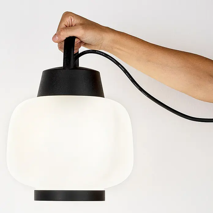 Forlight Portalámparas colgante Lamtam - 15 W, Ø x Al: 24 x 32 cm, Blanco/Negro, E27 - Una mano sostiene una lámpara blanca moderna con detalles negros sobre un fondo neutro. La lámpara emite un brillo suave.