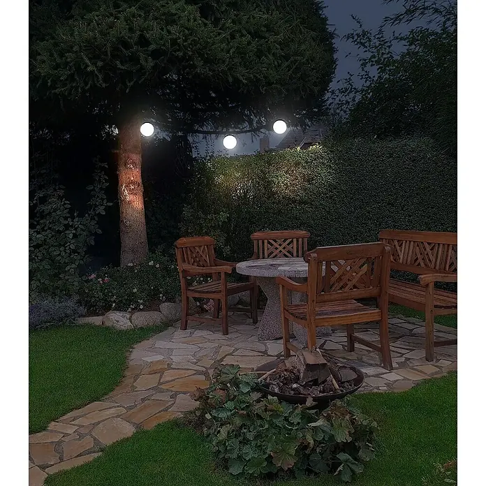 Forlight Proyector LED solar Bob - IP44 - Una acogedora zona de estar en el jardín con mesa y sillas de madera bajo guirnaldas de luces.