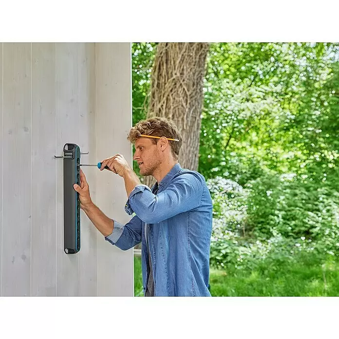 Gardena Combisystem Geräteleiste Flex - Passend für: GARDENA combisystem Geräte und Stiele - Mann montiert eine dunkelgraue und türkisfarbene Wandhalterung mit Schraubenzieher an einer hellen Holzwand.