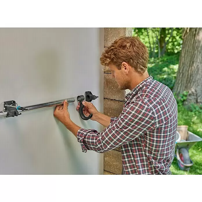 Gardena Halterung Plus - Traglast: 10 kg - Mann installiert ein modulares Wandhalterungssystem, indem er eine silberne Metallstange in eine schwarze Kunststoffhaken- und Schieneneinheit einfügt.