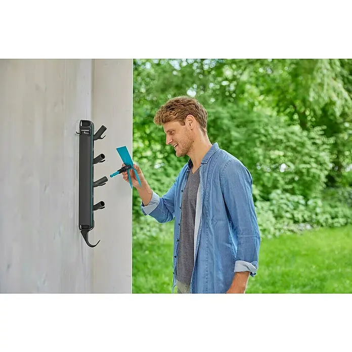 Gardena Halterung Einzelstecker Flex - Passend für: GARDENA combisystem, das Original GARDENA System & Scheren - Ein Mann befestigt ein Gardena-Bewässerungsprodukt an einer Wandhalterung. Das System bietet eine praktische Aufbewahrungslösung für Gartengeräte.