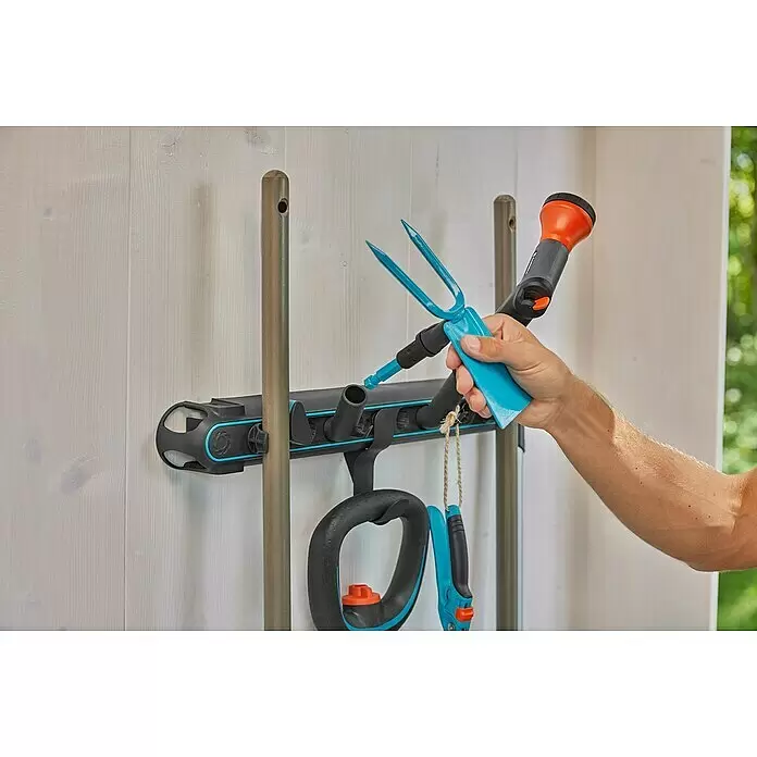 Gardena Halterung Einzelstecker Flex - Passend für: GARDENA combisystem, das Original GARDENA System & Scheren - Eine Hand platziert blaue Gartengeräte in ein grau-blaues, wandmontiertes Gerätehalter, das weitere Gartenwerkzeuge hält.