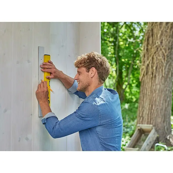 Gardena Combisystem Geräteleiste Flex - Passend für: GARDENA combisystem Geräte und Stiele - Mann verwendet eine Wasserwaage und einen Bleistift, um auf einer weißen Wand zu markieren, während er lächelt. Das gelbe Werkzeug ist gut sichtbar.