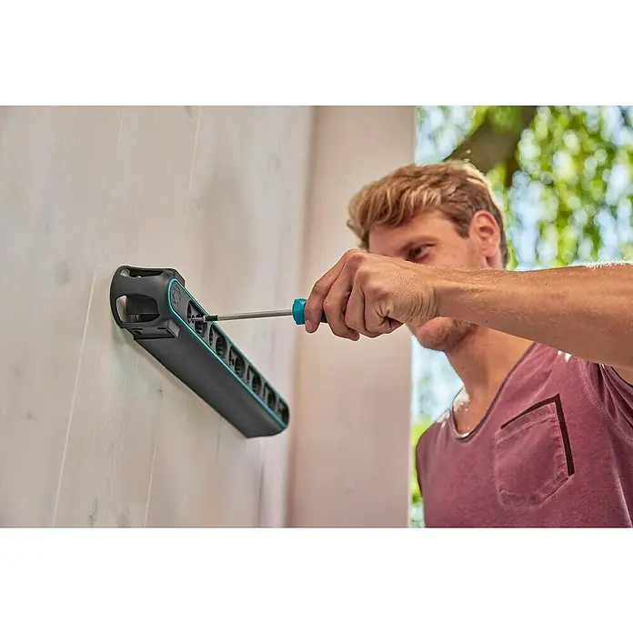 Gardena Halterung Flex - 10 kg, Kunststoff - Ein Mann befestigt eine Gardena Wandhalterung mit einem Schraubenzieher an einer weißen Wand, die für Gartengeräte gedacht ist.