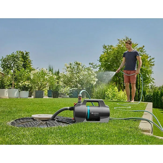 Gardena Gartenpumpe 4100 Silent Set - 550 W, Max. Fördermenge: 4.100 l/h - Ein Mann bewässert seinen Garten mit einer Gardena Gartenpumpe. Die Pumpe ist mit einem Schlauch an einer unterirdischen Wasserquelle angeschlossen.