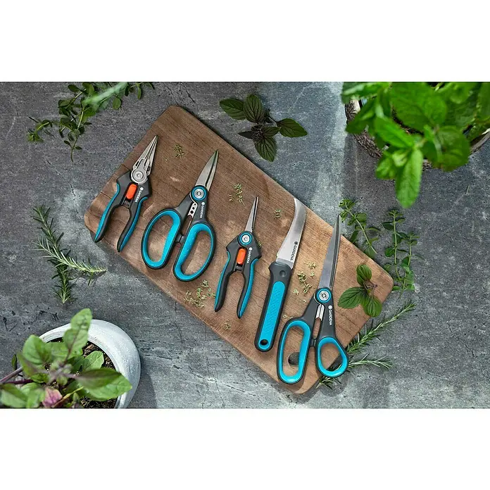 Gardena Universalschere MultiCut - Länge: 22,6 cm - Gartenscheren-Set von Gardena auf einem Holzbrett, umgeben von Grünpflanzen. Ideal für präzise Gartenarbeit und Pflanzenpflege mit hochwertigen Werkzeugen.