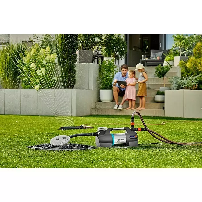 Gardena Gartenpumpe 6300 SilentComfort - 1.050 W, Max. Fördermenge: 6.300 l/h, Max. Förderhöhe: 49 m - Gardena Hauswasserautomat und Regner bewässern einen Rasen, Familie im Hintergrund.