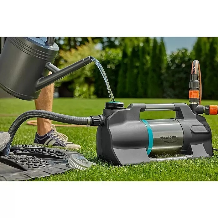 Gardena Gartenpumpe 5600 Silent+ - 900 W, Max. Fördermenge: 5.600 l/h - Grau/silberne Gardena 5600 Silent+ Pumpe auf Rasen, mit Wasser aus einer grauen Gießkanne befüllt. Ein schwarzer Wellschlauch ist angeschlossen.