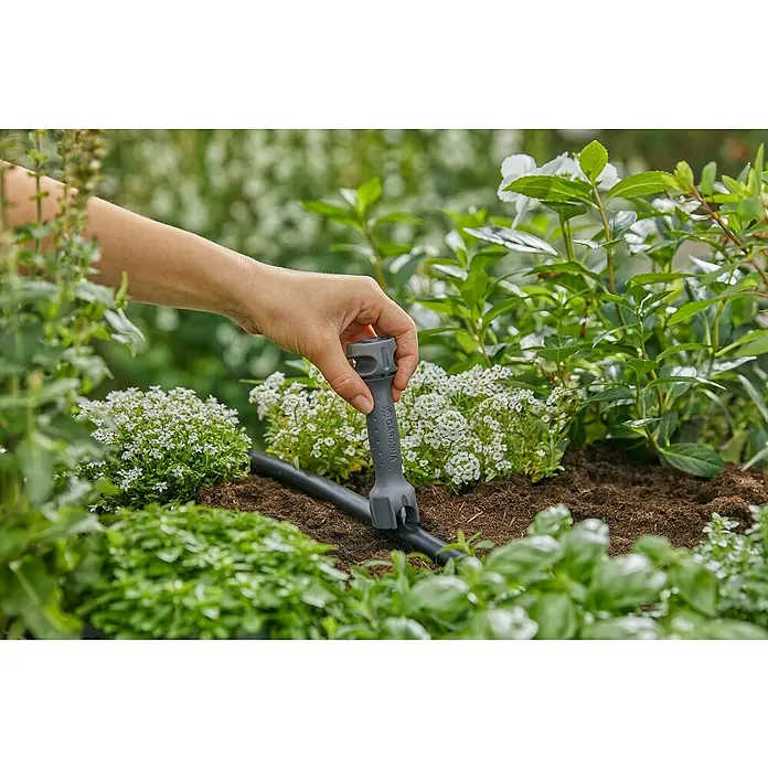 Gardena Micro-Drip Vorstecher - Passend für: Gardena Micro-Drip Artikel & Lochung des Verlegerohres, Kunststoff, Schwarz - Eine Hand führt ein Gardena-Werkzeug zum Verbinden eines Bewässerungsschlauchs in einem üppigen Garten ein.