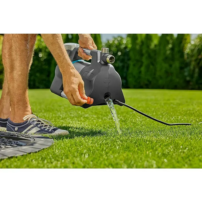 Gardena Gartenpumpe 5600 Silent+ - 900 W, Max. Fördermenge: 5.600 l/h - Nahaufnahme einer Gardena Gartenpumpe, die von einer Person entleert wird, mit Wasser, das auf grünes Gras fließt.