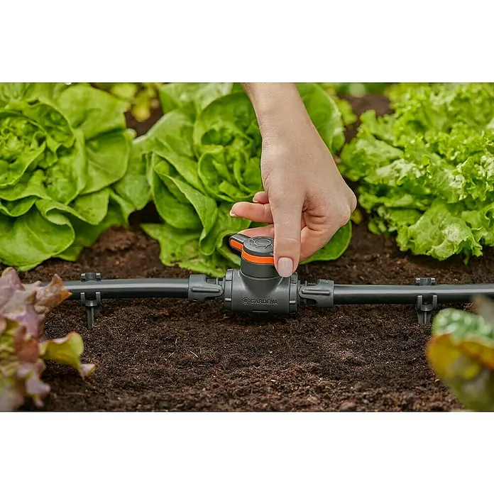 Gardena Micro-Drip Válvula de regulación 13 mm (1/2") - 13 mm, Plástico - Primer plano de una mano girando una válvula de cierre Gardena Micro-Drip-System, instalada en un parterre con lechugas.