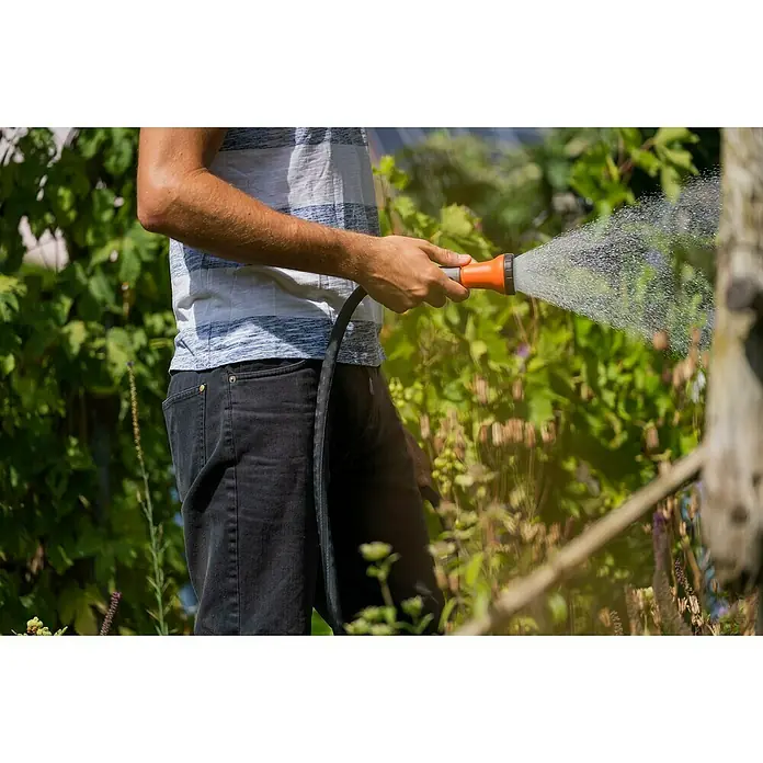 Gardena Gartenschlauch Liano Life - 10 m, Schlauchdurchmesser: 13 mm - Eine Person gießt mit einem orangefarbenen Gartenschlauch Pflanzen, wobei der Wasserstrahl deutlich zu sehen ist.