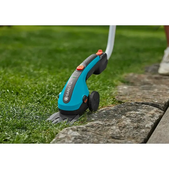 Gardena ClassicCut Podadora de batería - 3,6 V, Iones de litio, 1 batería, Anchura de la hoja: 8 cm - Primer plano de unas tijeras de césped inalámbricas Gardena en el borde del césped, que permiten recortar con precisión y garantizan un jardín bien cuidado.