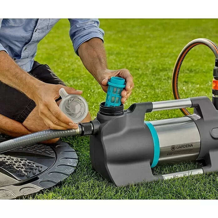 Gardena Gartenpumpe 6300 SilentComfort - 1.050 W, Max. Fördermenge: 6.300 l/h, Max. Förderhöhe: 49 m - Hände setzen einen blauen Filter in eine Gardena Wasserpumpe ein, während sie eine transparente Kappe halten. Ein grauer Schlauch ist angeschlossen.