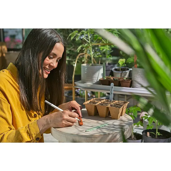 Gardena Scheren-Set FreshCut mit Kräuterschilder - 4 -tlg. - Eine Frau beschriftet Pflanzenschilder für ein Set mit biologisch abbaubaren Pflanztöpfen, um einen nachhaltigen Garten zu beginnen.