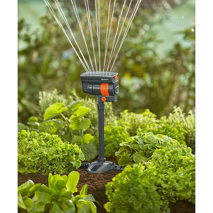 Gardena Micro-Drip Tubo prolongador para OS 90 - 2 ud., Largo: 20 cm - Imagen de un aspersor multisuperficie Gardena en funcionamiento en el jardín, regando un césped. El producto es gris oscuro y naranja.