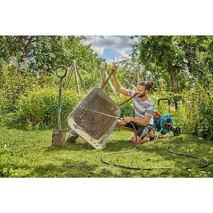 Gardena Gartenschlauch Liano Life - 10 m, Schlauchdurchmesser: 13 mm - Ein Mann reinigt eine schmutzige Schubkarre mit einem Gardena-Gartenschlauch auf einer grünen Wiese, während ein Spaten daneben steht.
