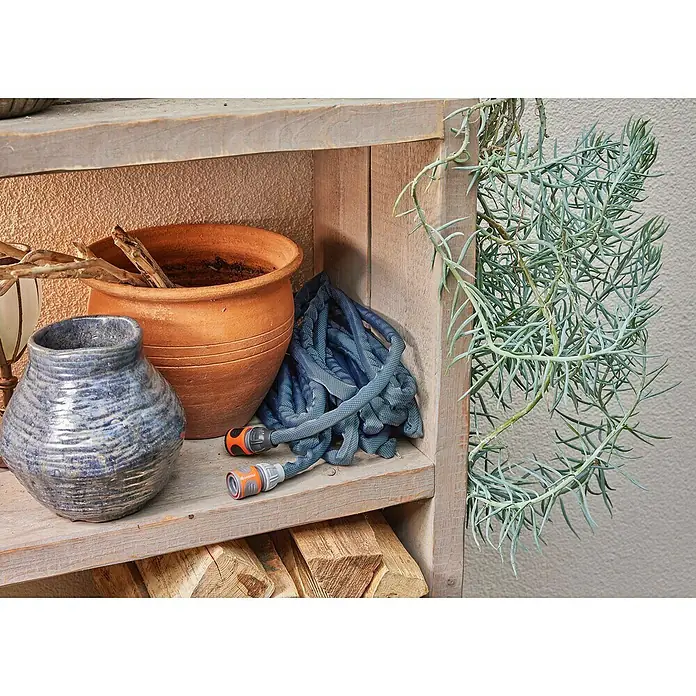 Gardena Gartenschlauch Liano Xtreme Set mit Wandschlauchhalter - Länge: 15 m - Aufnahme einer grauen, expandierenden Gartenschlauchrolle von Gardena, die ordentlich auf einem Holzregal mit anderen Gartengeräten verstaut ist.