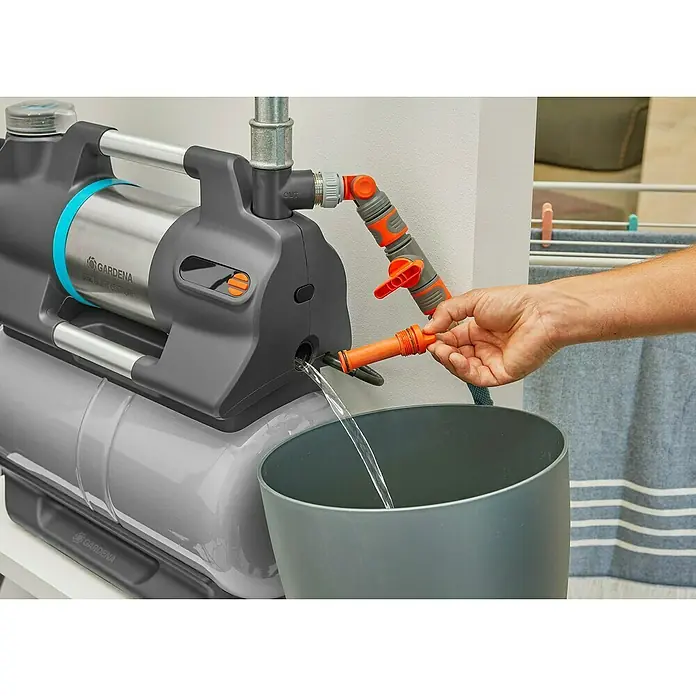 Gardena Hauswasserwerk 5600 Silent Comfort - 650 W, Max. Fördermenge: 5.600 l/h, Max. Druck: 4,7 bar - Gardena Hauswasserwerk, mit dem eine Person gerade einen Schlauch anschließt, während Wasser in einen Eimer abgeleitet wird.