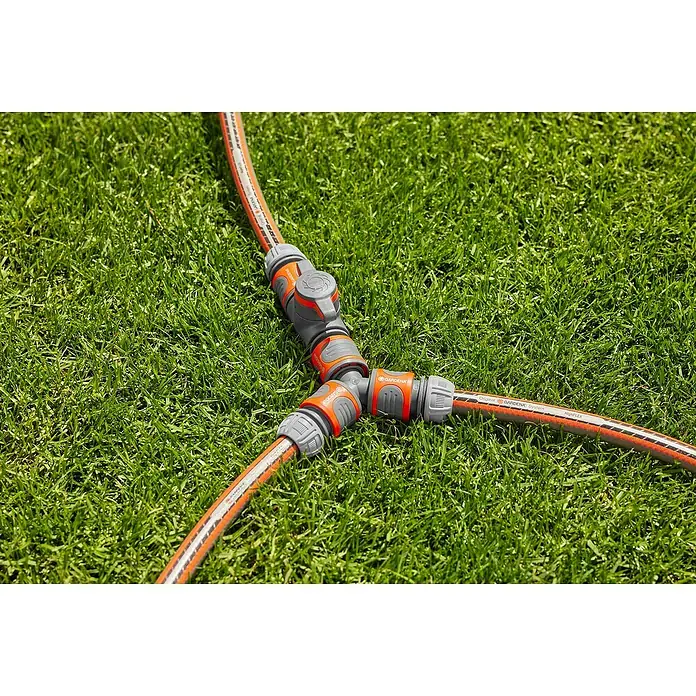 Gardena Regulierventil - Wasserdurchfluss einstellbar, Kunststoff - Gardena-Schlauchverbinder auf Rasen. Der Verbinder ist grau und orange und verbindet drei Schläuche miteinander. Praktische Gartenbewässerung.
