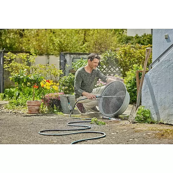 Gardena EcoLine Gartenschlauch - 20 m - Ein Mann reinigt einen großen grauen Topf im Freien mit einem schwarz-blauen Gartenschlauch und einer Sprühdüse, wobei ein feiner Wassernebel entsteht.