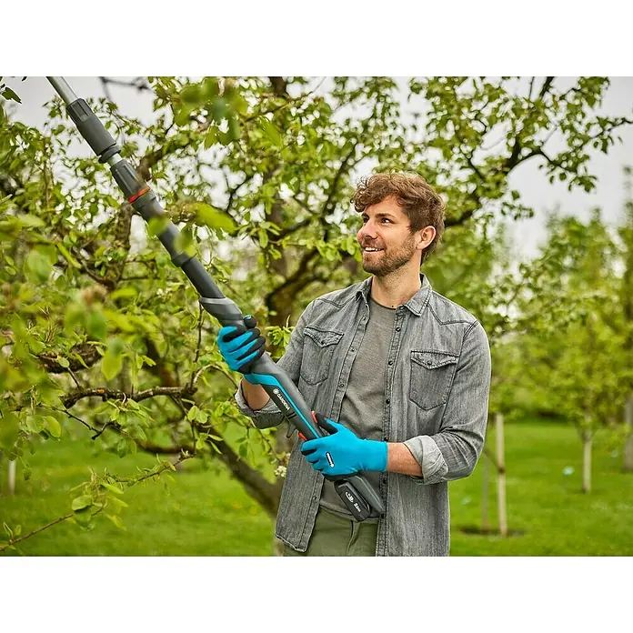 Gardena Power for All 18V Cortarramas de jardín HighCut - 18 V, Sin batería, Grosor de rama máx.: 28 mm, Largo: 255,7 cm - Un hombre usa una podadora a batería Gardena para recortar ramas, con guantes.