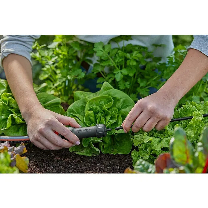 Gardena Micro-Drip Hahnanschlussstück - 3/16" x 4,6 mm - Nahaufnahme einer Person, die ein GARDENA Micro-Drip-System in einem Garten mit Salat und Kräutern installiert. Bewässerung leicht gemacht.
