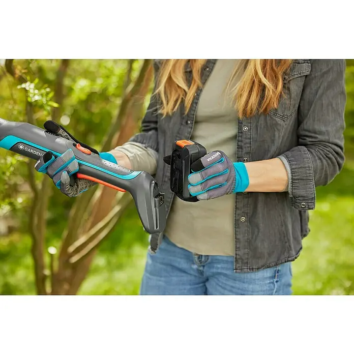 Gardena Power for All 18V Cortarramas de jardín - 18 V, Sin batería, Grosor de rama máx.: 32 mm - La persona inserta la batería en unas tijeras inalámbricas para césped y arbustos Gardena. La herramienta es gris claro, azul y naranja.
