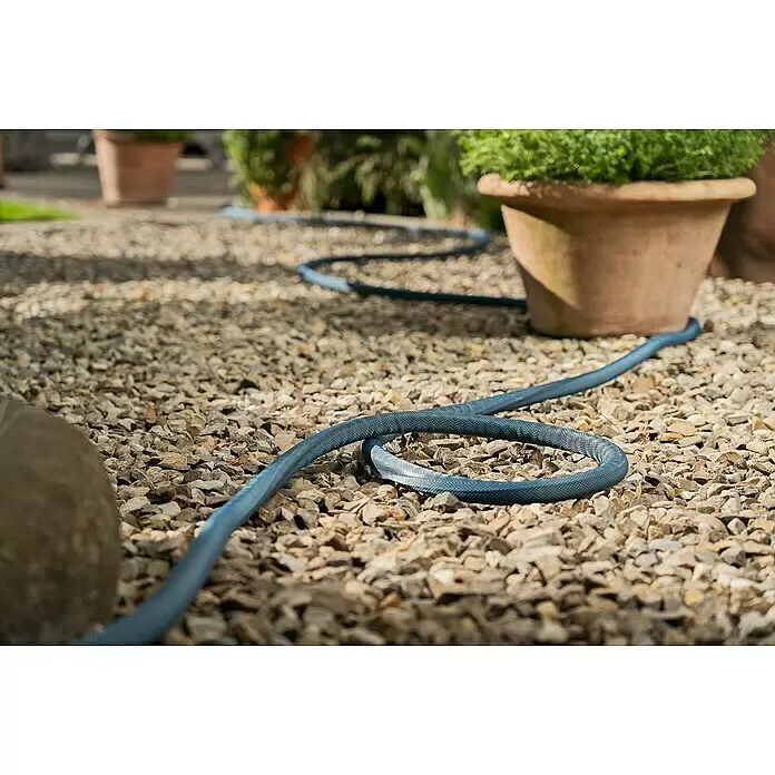 Gardena Gartenschlauch Liano Xtreme Set - 30 m, Schlauchdurchmesser: 19 mm - Blauer, stoffummantelter Gartenschlauch liegt auf einem Kiesweg, der zu einer Topfpflanze führt.