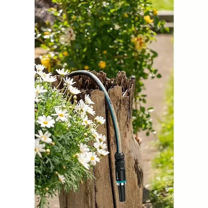 Gardena EcoLine Gartenschlauch Set - 20 m, Ausstattung: Anschlussstücke - Gardena EcoLine Gartenschlauch mit Anschlussstück und Brause, auf einem Baumstumpf zwischen weißen Blumen.