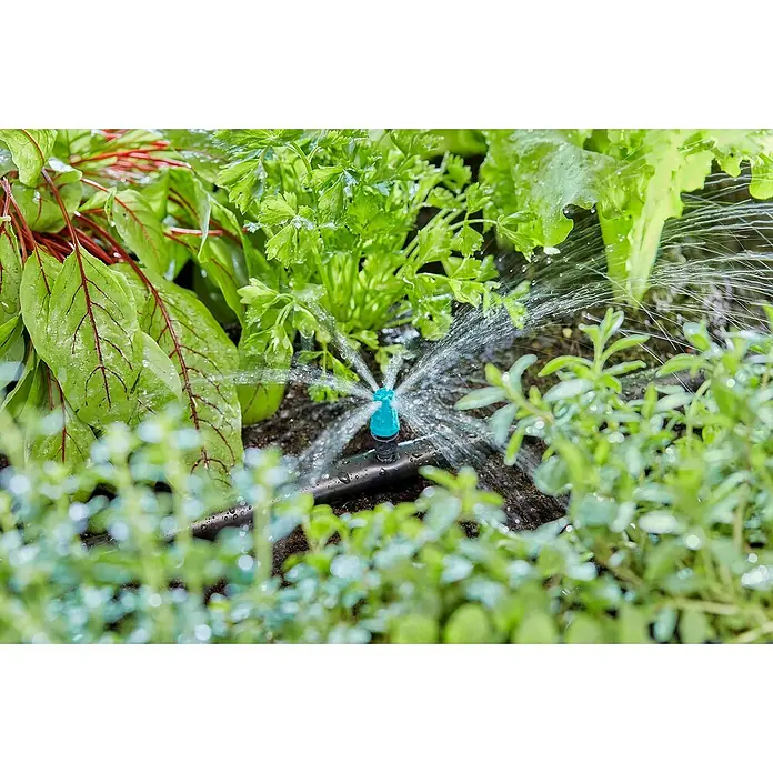 Gardena Micro-Drip Kleinflächendüse - 10 Stk., 1/2" x 13 mm - Nahaufnahme eines kleinen, blauen Bewässerungs-Sprinklers, der inmitten grüner Pflanzen und Erde in einem Garten Wasser versprüht.
