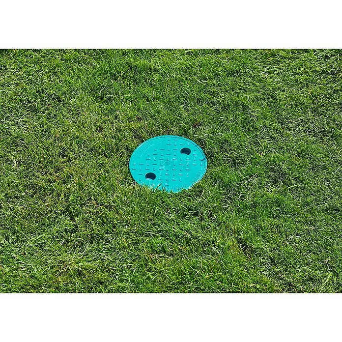Gardena Sprinklersystem Druckminderer - 1″ - Runde, türkisfarbene Bewässerungsventil-Box aus Kunststoff, eingebettet in einen grünen Rasen mit zwei Löchern zum Öffnen.