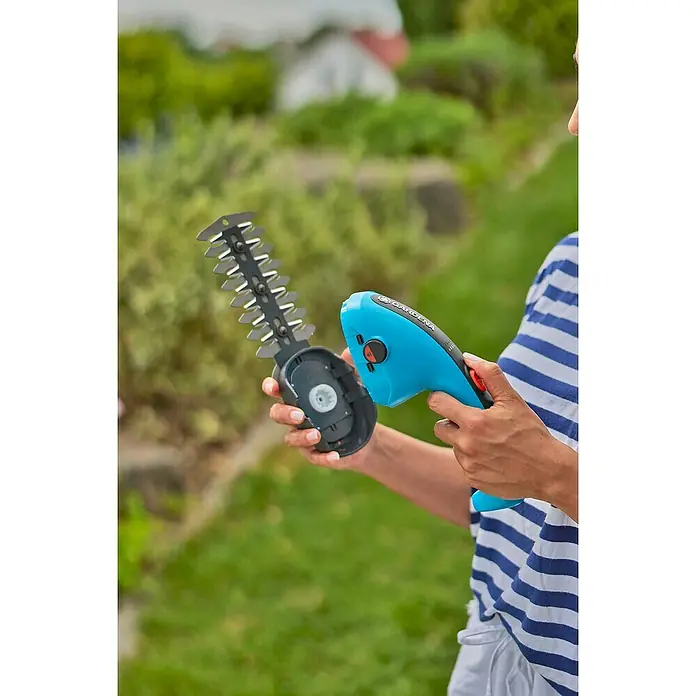 Gardena ComfortCut Akku-Gras- & Strauchschere LI - 3,6 V, Li-Ionen, 1 Akku, Schwertbreite: 8 cm - Eine Person, die eine Gardena Akku-Grasschere mit Messern in einem Garten hält.