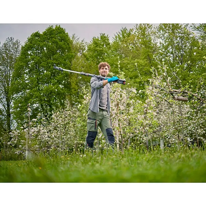 Gardena Power for All 18V Cortarramas de jardín HighCut 360/18V P4A - 18 V, Sin batería, Grosor de rama máx.: 28 mm, Largo: 360 cm - Un hombre usando una podadora de altura inalámbrica Gardena para recortar un árbol en un exuberante jardín verde, rodeado de naturaleza.