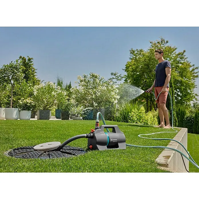 Gardena Gartenpumpen-Set 4200 Silent600 W, Max. Fördermenge: 4.200 l/h - Der Gardena Hauswasserautomat 4000/5 eco im Einsatz: Ein Mann bewässert seinen Garten mit dem Hauswasserwerk, das auf dem Rasen steht.