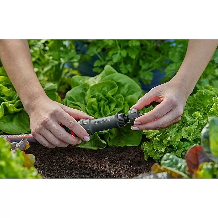Gardena Micro-Drip Hahnanschlussstück - 3/16" x 4,6 mm - Hände verbinden eine graue Gardena Bewässerungsschlauchkupplung inmitten von Gartenpflanzen.