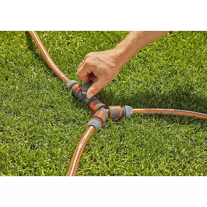 Gardena Regulierventil - Wasserdurchfluss einstellbar, Kunststoff - Eine Hand verstellt einen grau-orangen Y-Schlauchverbinder mit Ventilen, der drei Gartenschläuche verbindet.