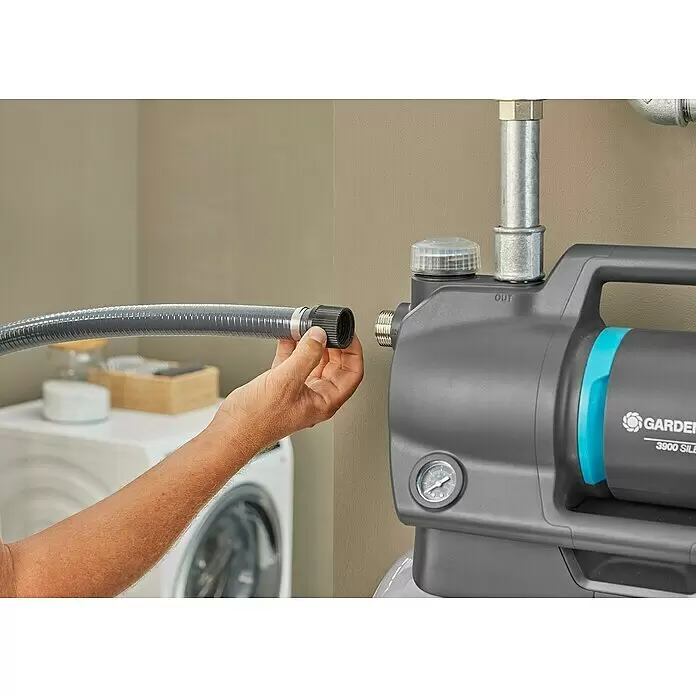 Gardena Hauswasserwerk 3900 Silent - 650 W, Max. Fördermenge: 3.900 l/h, Max. Druck: 4,3 bar - Eine Hand verbindet einen grauen gerippten Schlauch mit dem "IN"-Anschluss einer grauen Gardena Wasserpumpe mit blauen Akzenten.