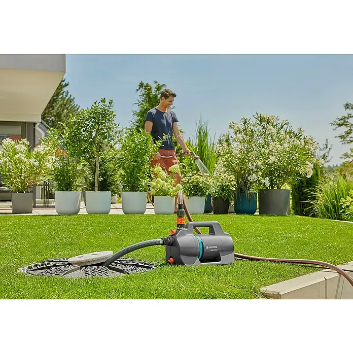 Gardena Gartenpumpe 4300 Silent - 650 W, Max. Fördermenge: 4.300 l/h - Ein Mann bewässert Pflanzen im Garten mit der Gardena Gartenpumpe 4000/4. Die Pumpe ist auf dem Rasen neben einer Wasserquelle platziert.
