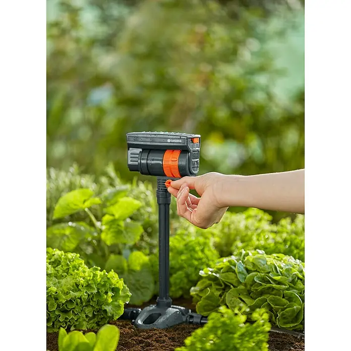 Gardena Micro-Drip Tubo prolongador para OS 90 - 2 ud., Largo: 20 cm - Primer plano de un aspersor oscilante Gardena Viereck Viva con una mano ajustando un ajuste, en un jardín.