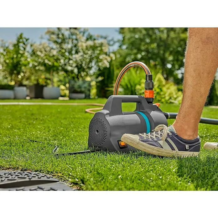 Gardena Gartenpumpe 4200 Silent - 600 W, Max. Fördermenge: 4.200 l/h - Eine graue Gardena Gartenpumpe steht auf dem Rasen, ein Bein mit einem Turnschuh berührt die Pumpe.
