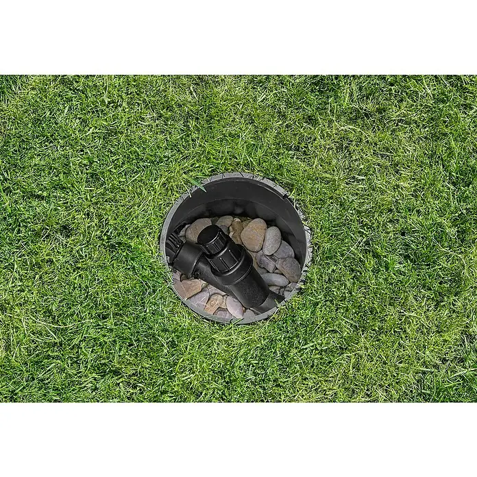 Gardena Sprinklersystem Druckminderer - 1″ - Ein schwarzer Bewässerungsanschluss mit Steinen in einem schwarzen Behälter, umgeben von saftigem, grünem Gras.