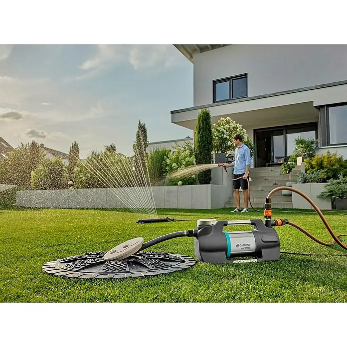Gardena Gartenpumpe 5600 Silent+900 W, Max. Fördermenge: 5.600 l/h - Das Bild zeigt eine GARDENA Gartenpumpe mit Bewässerungssystem und einem Mann, der den Garten bewässert.