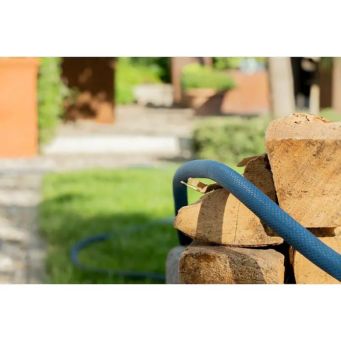 Gardena Gartenschlauch Liano Xtreme Set - 20 m, Schlauchdurchmesser: 19 mm - Nahaufnahme eines blauen Gartenschlauchs, der auf einem Stapel Holz liegt, mit einem verschwommenen Garten im Hintergrund.