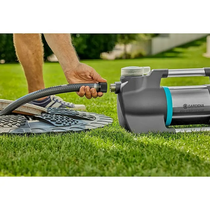 Gardena Gartenpumpe 6300 SilentComfort - 1.050 W, Max. Fördermenge: 6.300 l/h, Max. Förderhöhe: 49 m - Ein Mann schließt einen grauen Wasserschlauch an eine GARDENA 6300 Silent Comfort Gartenpumpe auf einer grünen Rasenfläche an.