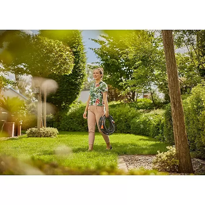 Gardena Gartenschlauch Liano Life - 10 m, Schlauchdurchmesser: 13 mm - Frau trägt einen aufgerollten schwarzen Gartenschlauch mit orangefarbenen Anschlüssen.