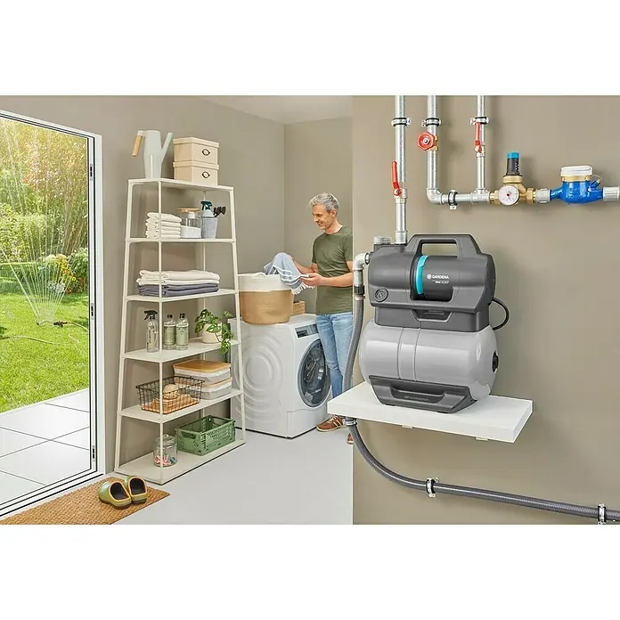 Gardena Grupo de presión 3900 Silent - 650 W, Capacidad de bombeo máx.: 3.900 l/h, Presión máx.: 43 bar - Imagen de un sistema doméstico de agua Gardena 3600/4E LCD con tuberías y conexiones, instalado en un lavadero.
